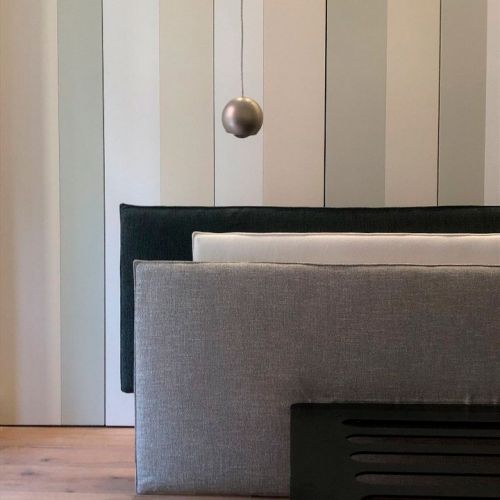 Pared empapelada con rayas, lámpara de techo gris y cojines grandes en tonos neutros