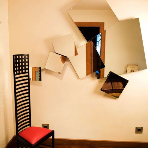 Detalle de rincón de habitación con silla roja de diseño y espejos irregulares