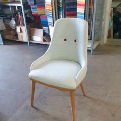 Silla blanca con patas de madera y paneles con telas de tapizado de colores detrás