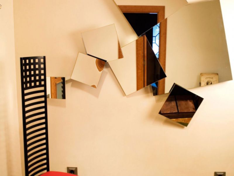 Detalle de rincón de habitación con silla roja de diseño y espejos irregulares